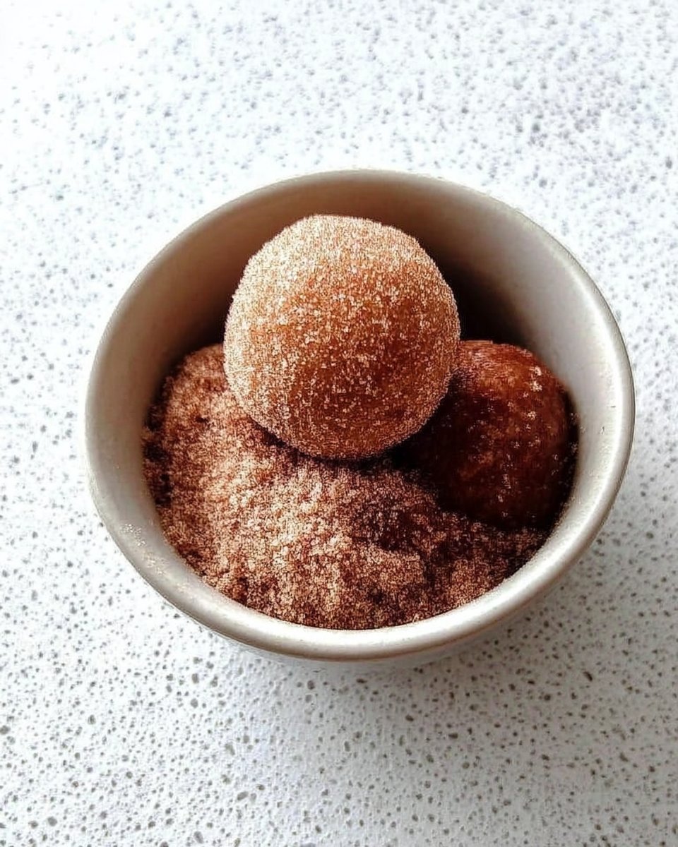 Cookie dough balls being rolled in a bowl of cinnamon and granulated sugar