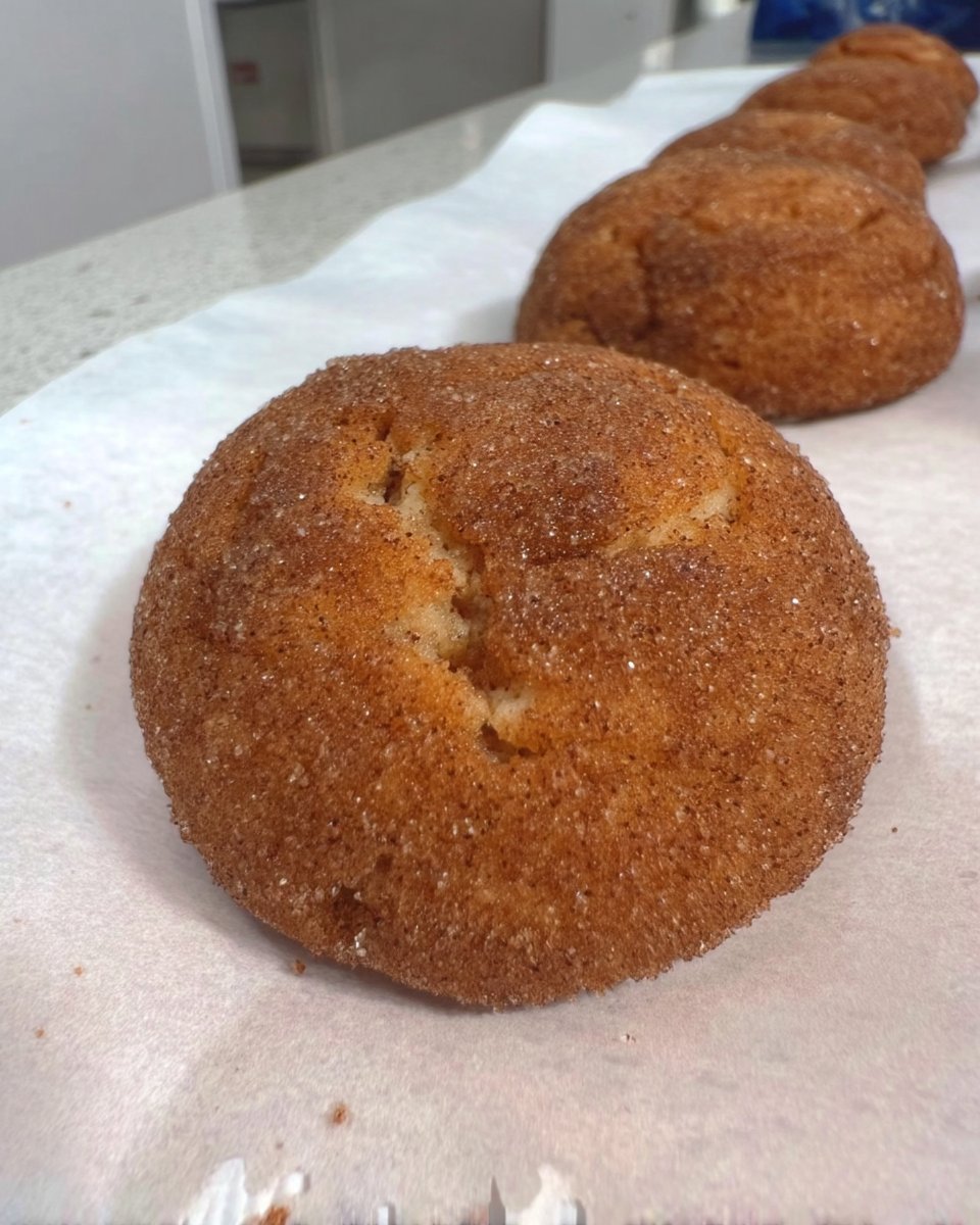 Freshly baked snickerdoodles cooling on a wire rack with a glass of milk.