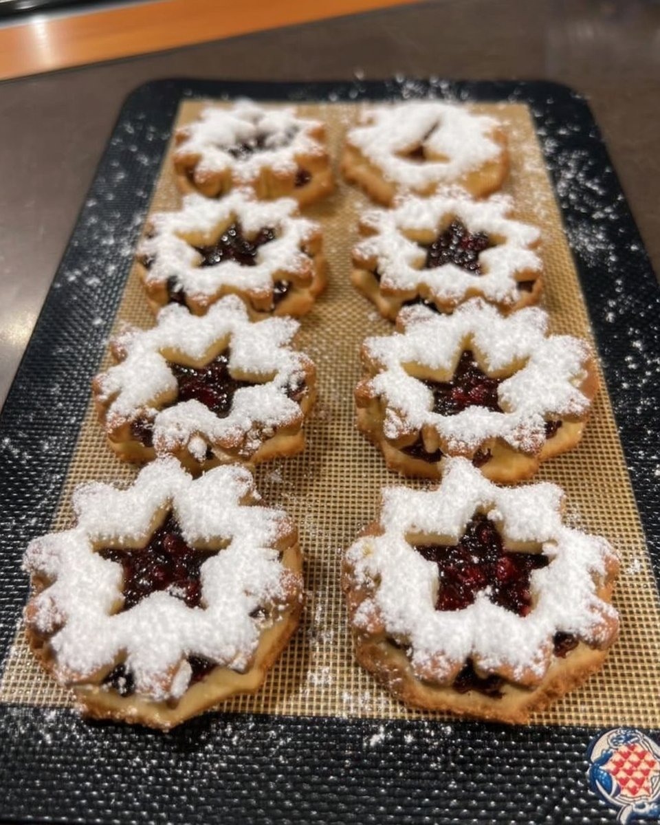 A stack of raspberry linzer cookies with powdered sugar and heart-shaped windows.