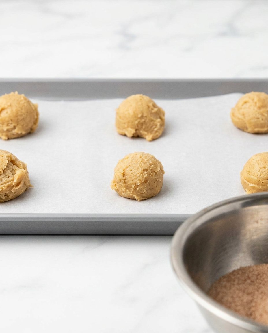 Hands rolling a ball of cookie dough in a bowl of cinnamon sugar
