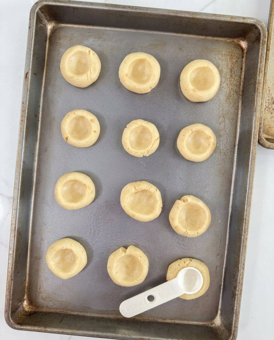 Hands pressing an indentation into cookie dough balls on a baking sheet